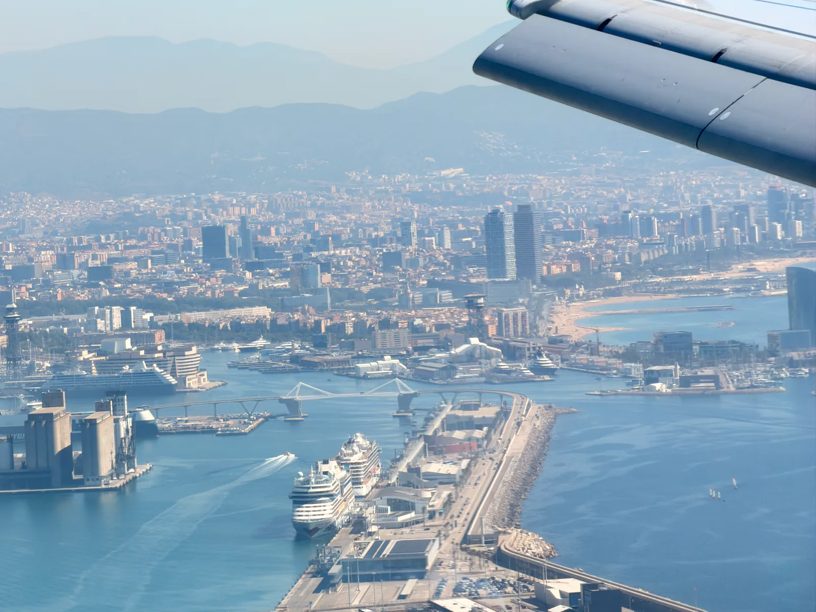 An aircraft wing over a coastal city, port and mountains
