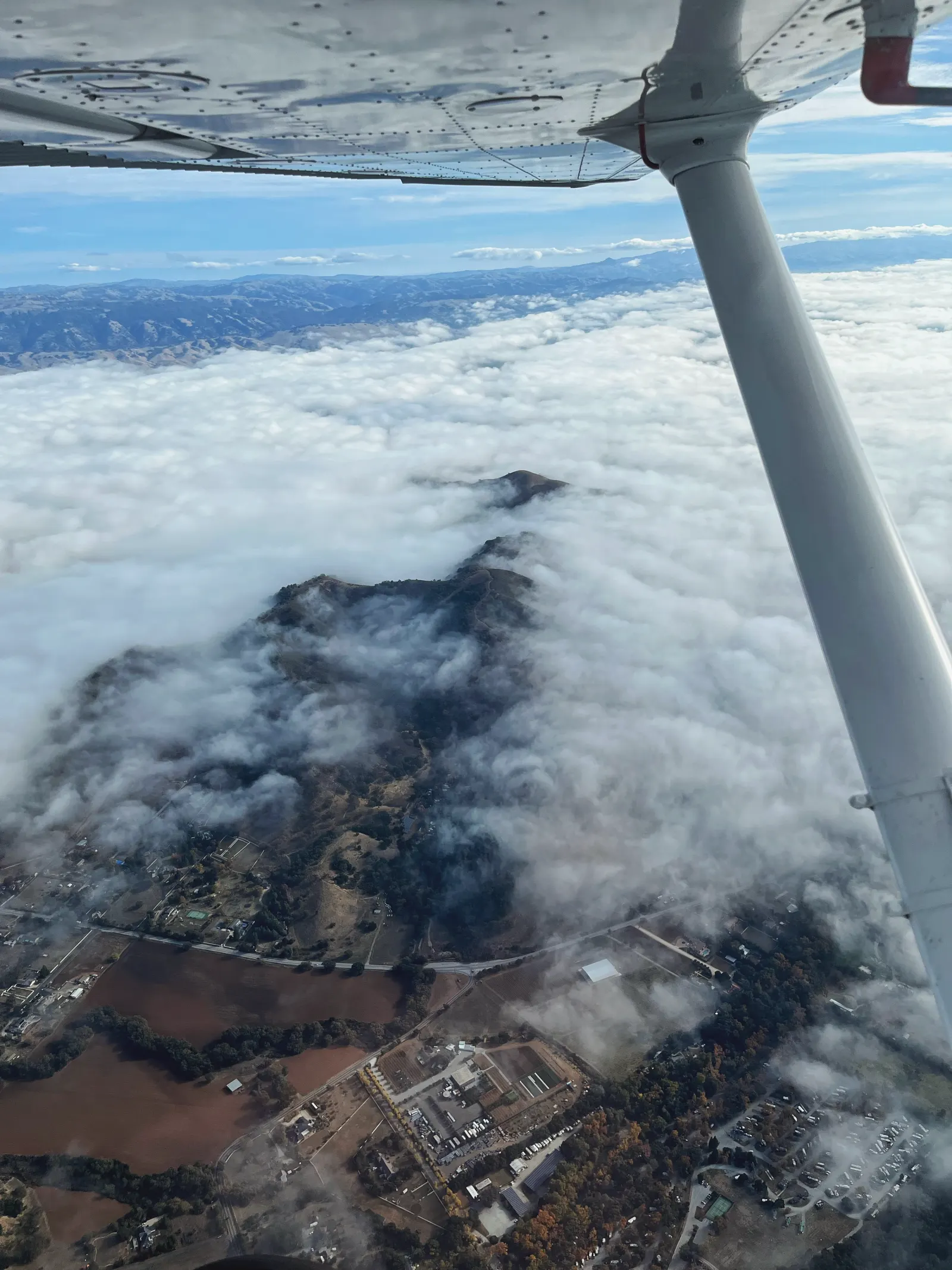 View from under a Cessna wing over low clouds and hills